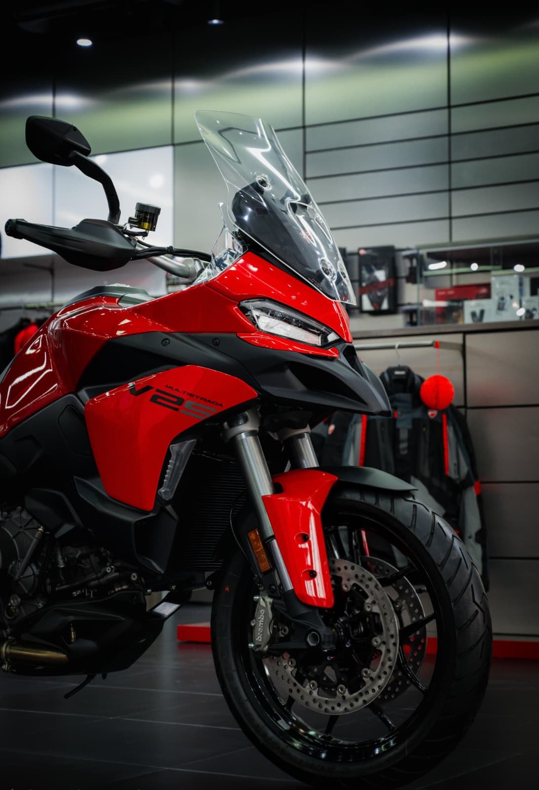 Multistrada V2 S Red en concesionario Ducati con motos y equipacion al fondo.